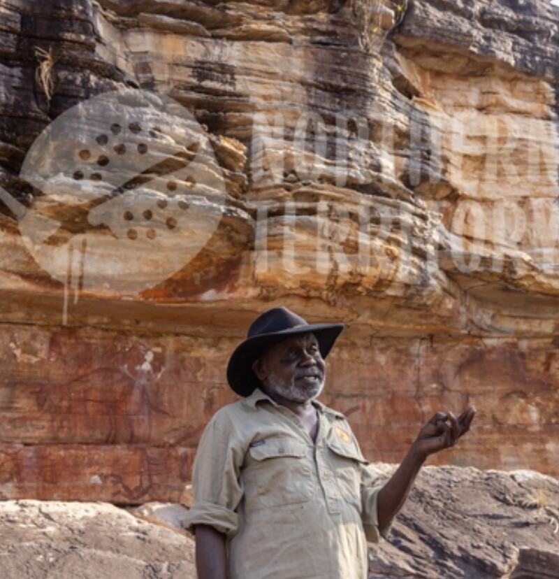 Kakadu Indigenous Senior Traditional Owner and Parks Ranger A Kakadu Indigenous Senior Traditional Owner And Parks Ranger Standing In Front Of Ancient Rock Art At Rock Art Site In Kakadu National Park.